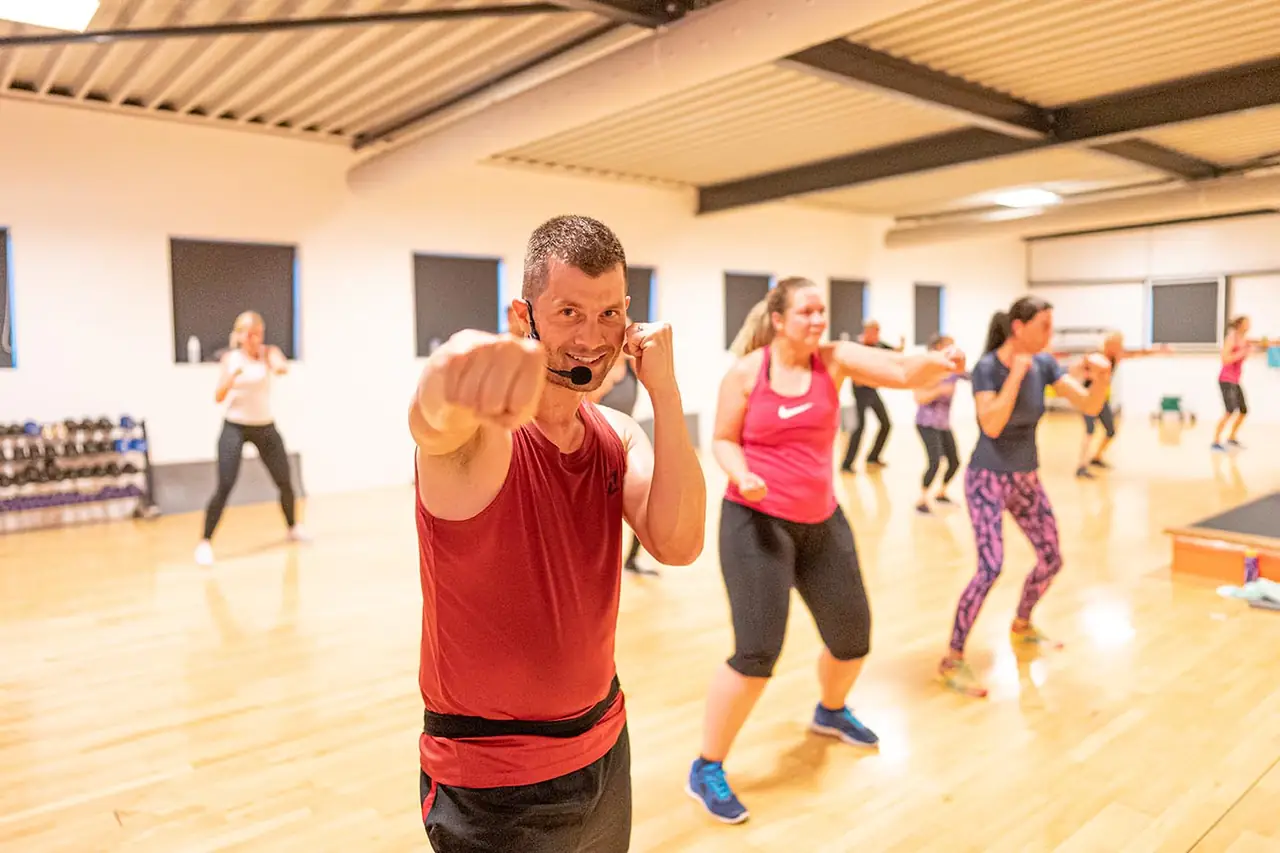 Bodycombatinstructeur stoot naar voren, de groep doet mee