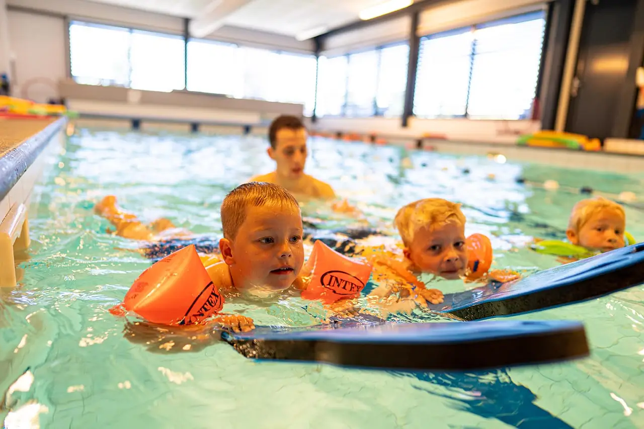 Groepje kinderen zwemt met drijfmiddelen tijdens zwemles