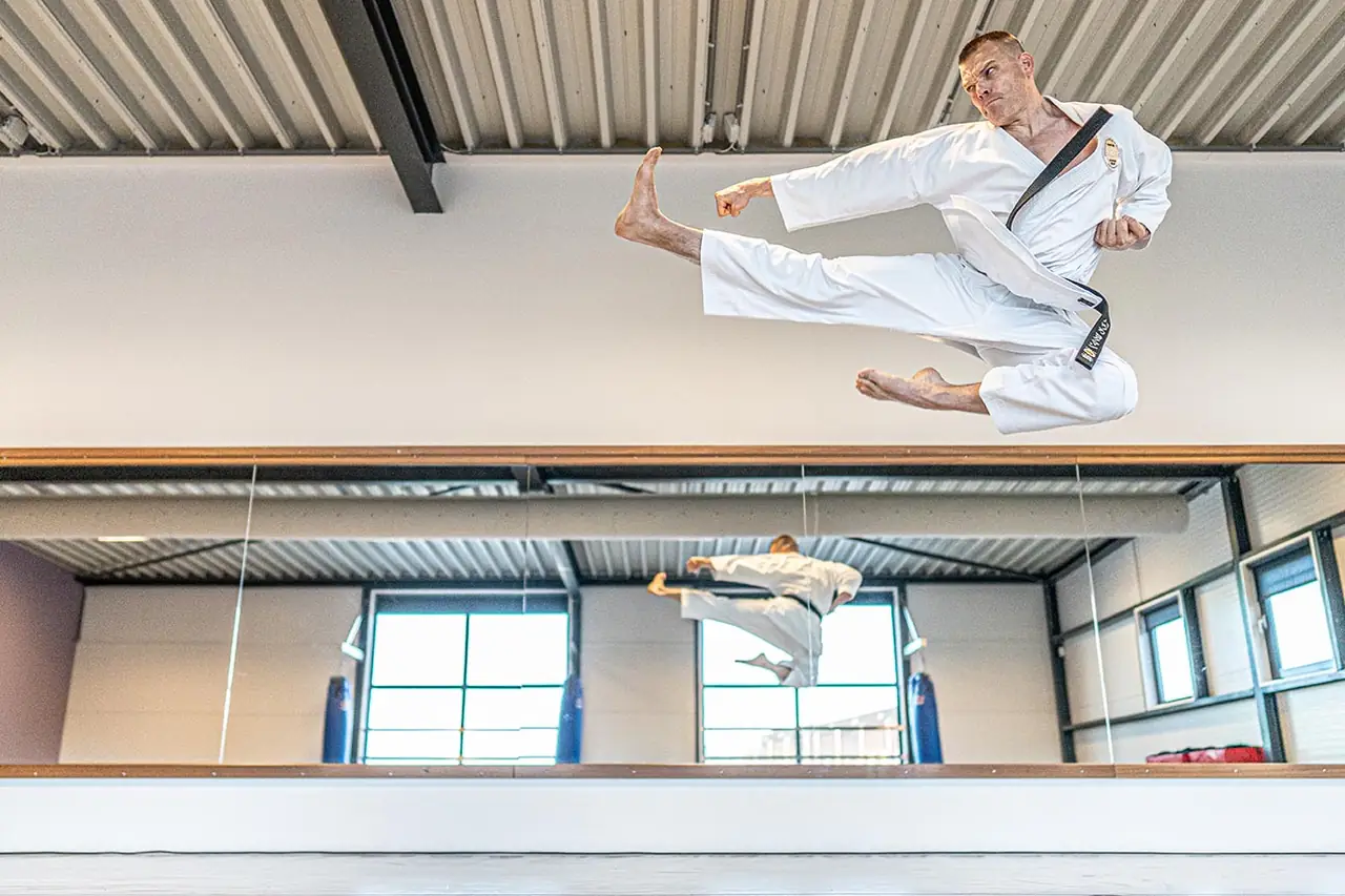 Karateka maakt een sprongtrap in de dojo