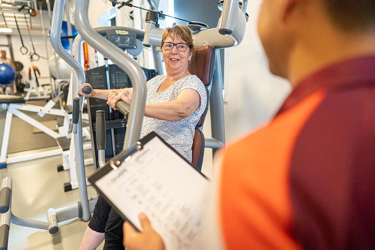 Instructeur begeleidt een oudere sporter op een fitnesstoestel